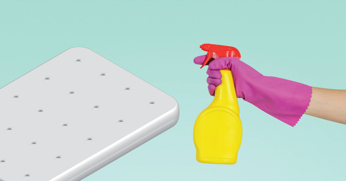 Hand wearing pink ruubber glove pointing a disinfecting spray bottle towards a mattress