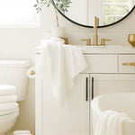 Bathroom with white fixtures, towels, and a round mirror.