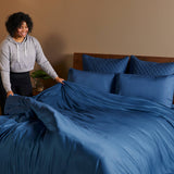 woman making a bed of dark indigo blue bamboo duvet cover with pillows on bed