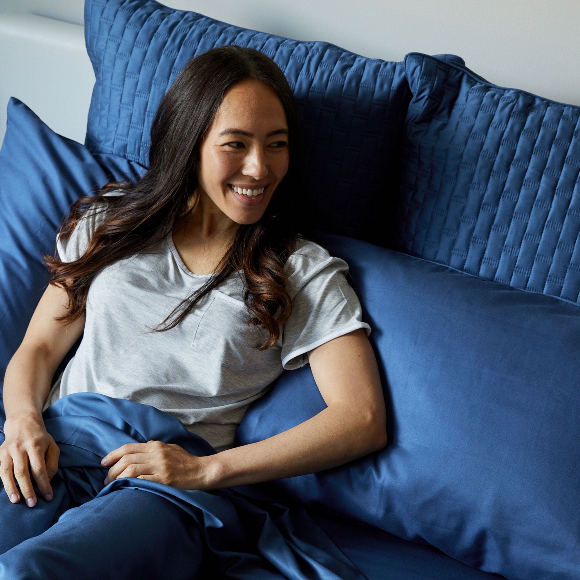 lady smiling in bed leaning on dark blue indigo bamboo pillows and shams
