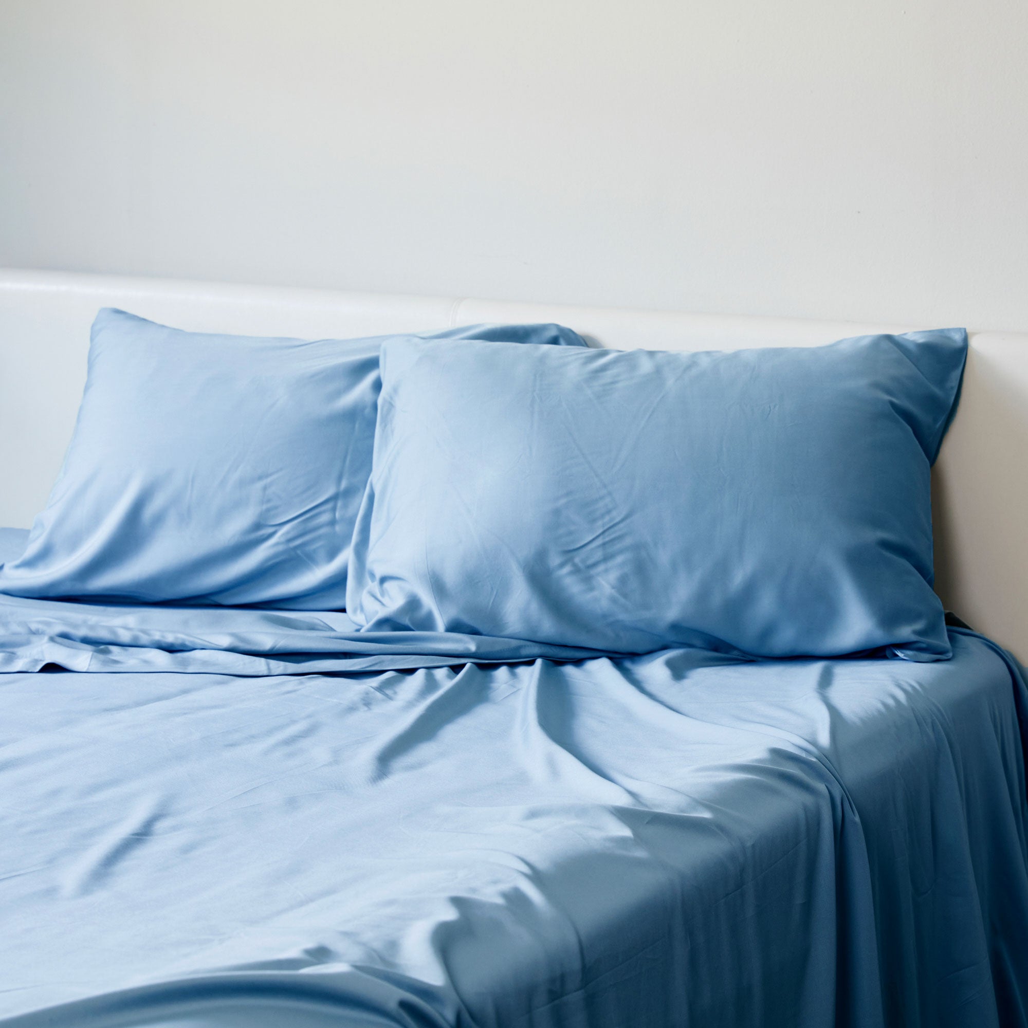 A set of blue bamboo pillowcases displayed on a bed, with two pillowcases stacked on top of each other and the bedsheet partially visible.