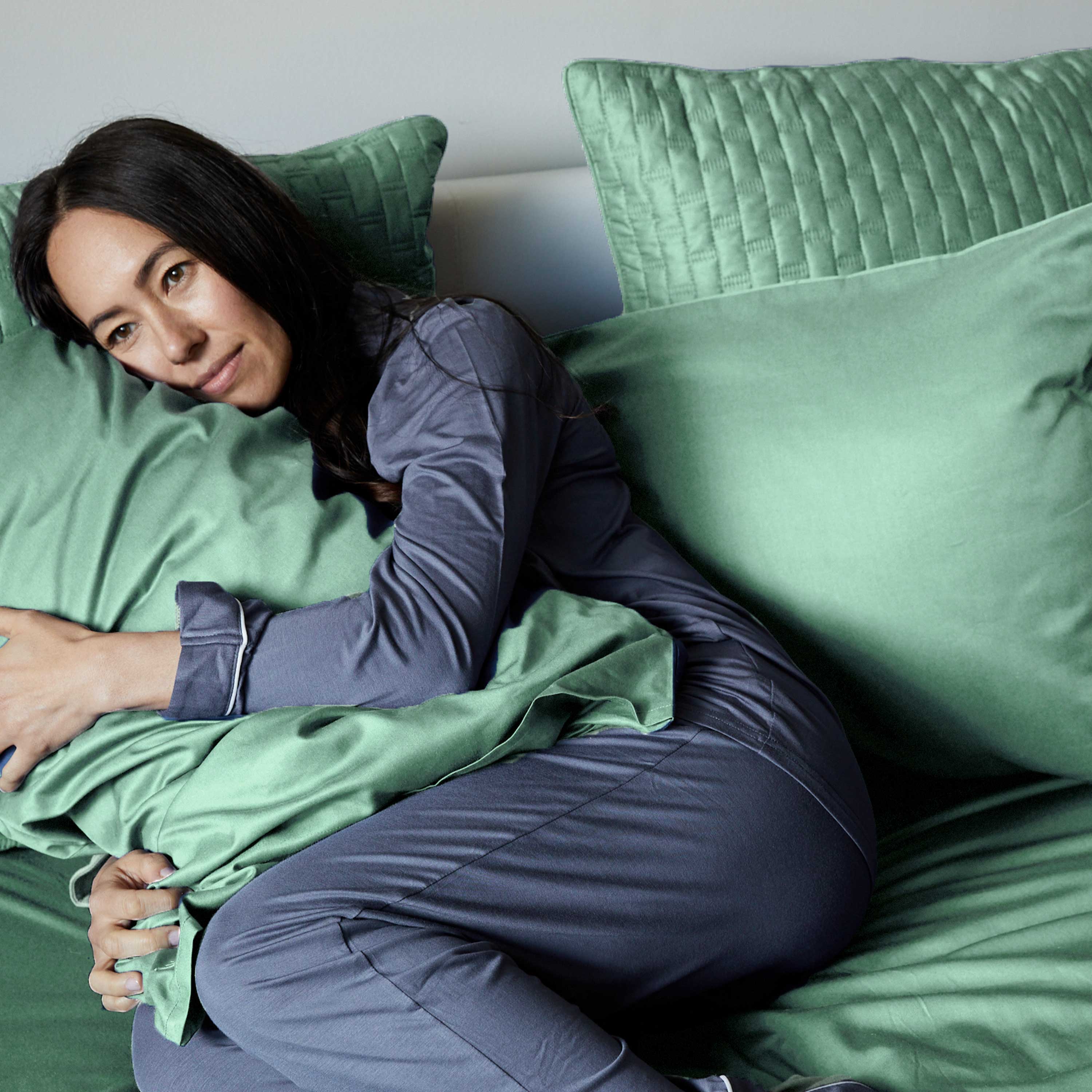 woman snuggling a seaglass green bamboo pillow laying in bed wearing gray pajamas