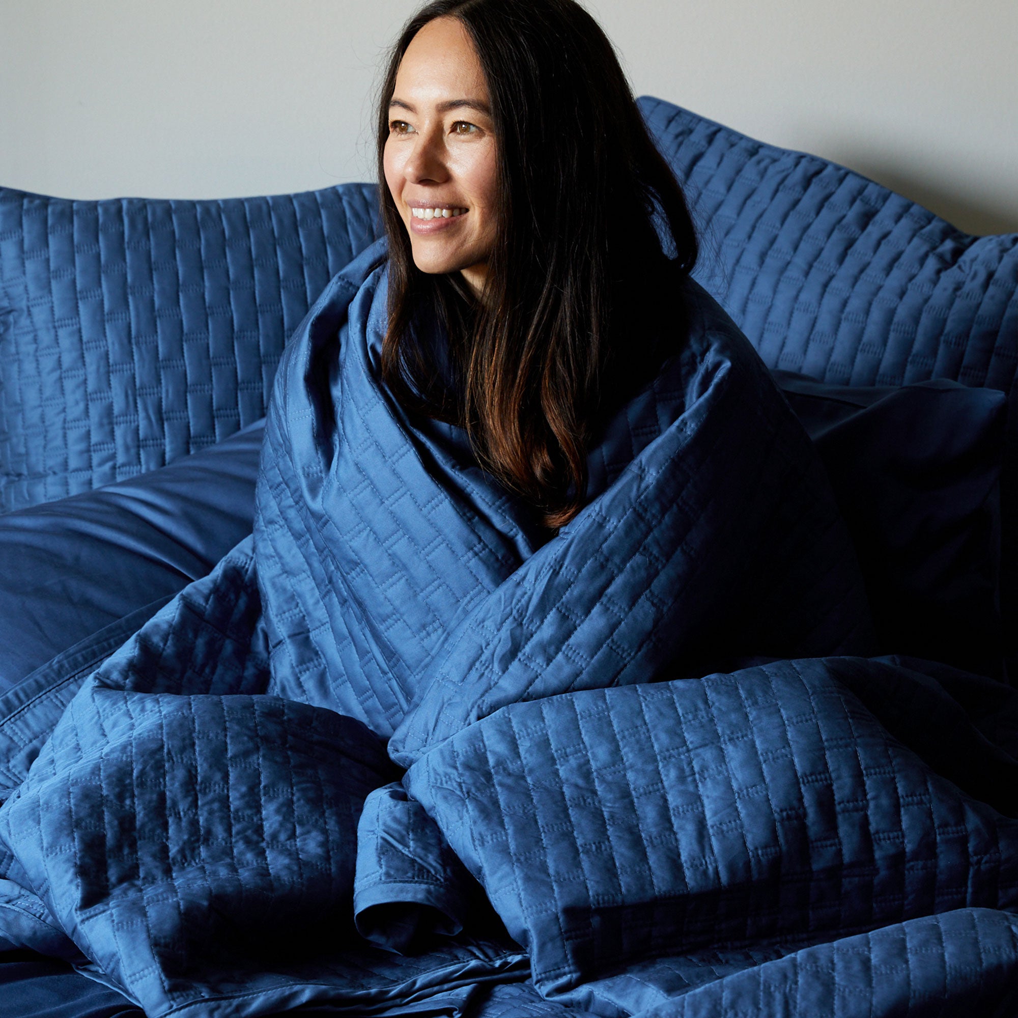 dark haired lady wrapped in dark blue indigo bamboo quilted coverlet on a bed