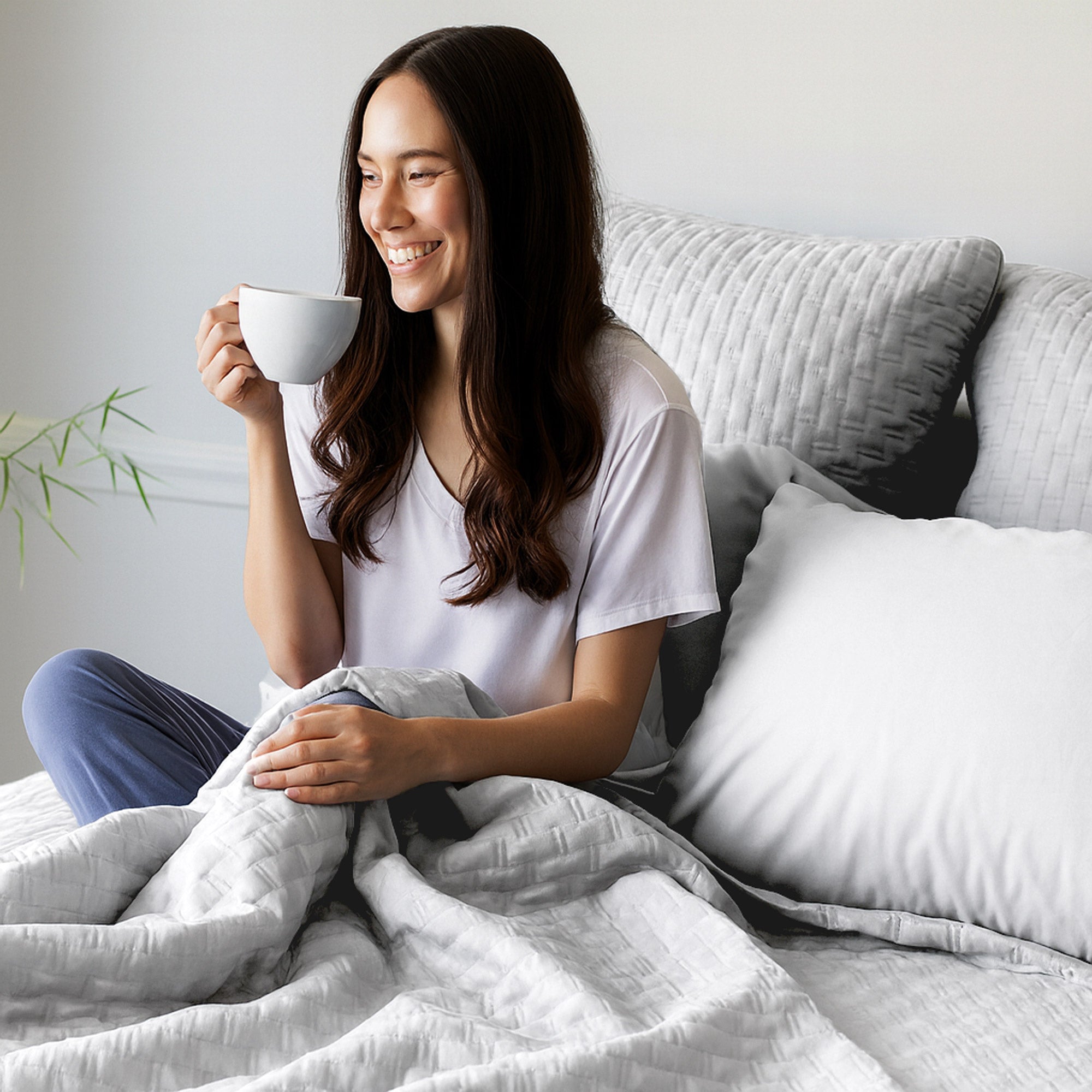 Woman sitting on a bed holding a mug, smiling.