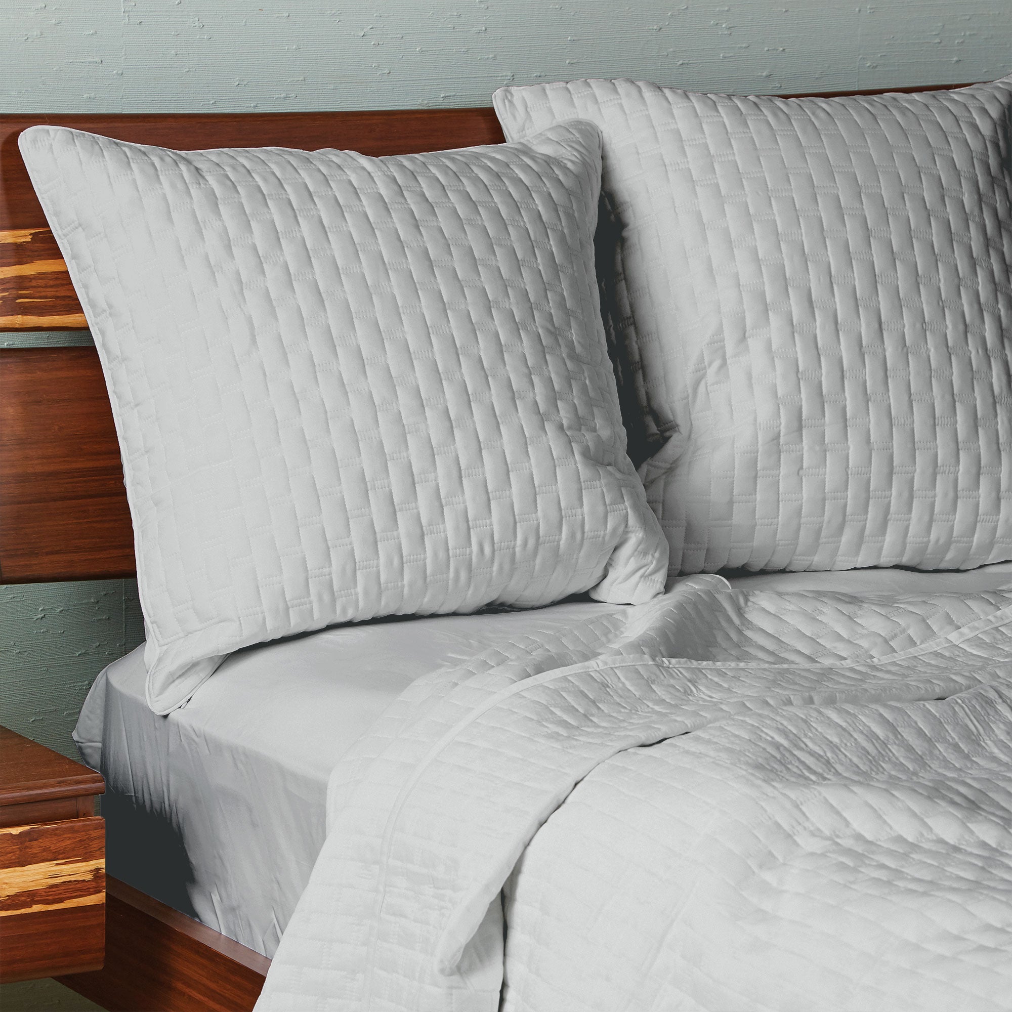 Two gray bamboo quilted euro shams on a bed, with a subtle quilted pattern and piped edges.