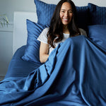 woman snuggling in bed leaning on pillows wrapped in dark indigo blue bamboo bed sheets