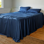 dark indigo blue luxury bamboo bed sheets made on a bed with pillows and woven rug