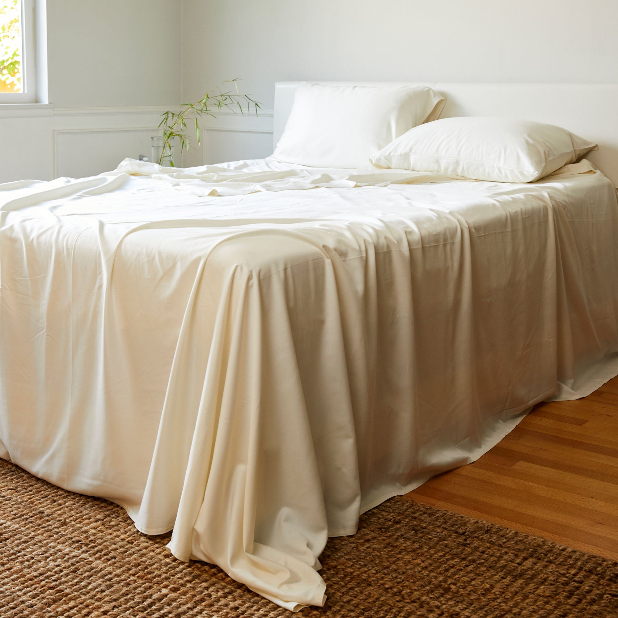 ivory bamboo bed sheets made on a bed with pillows and a woven rug on floor
