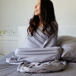 woman wrapped in silver gray platinum bamboo bed sheets made on a bed with pillows