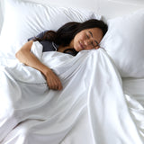 woman snuggled up in white silky bamboo bed sheets leaning against pillows