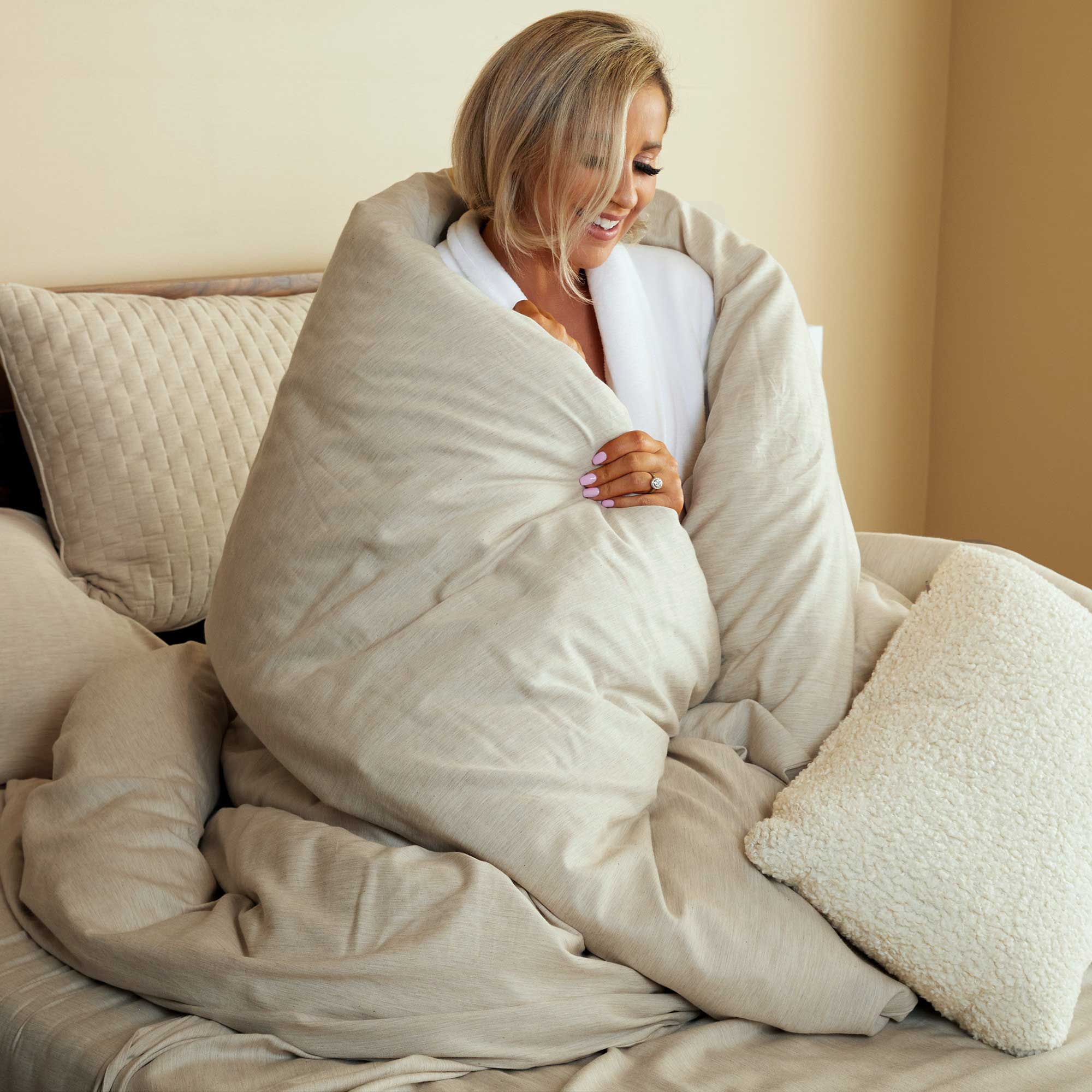woman wrapped up in sand beige bamboo duvet cover on a bed smiling