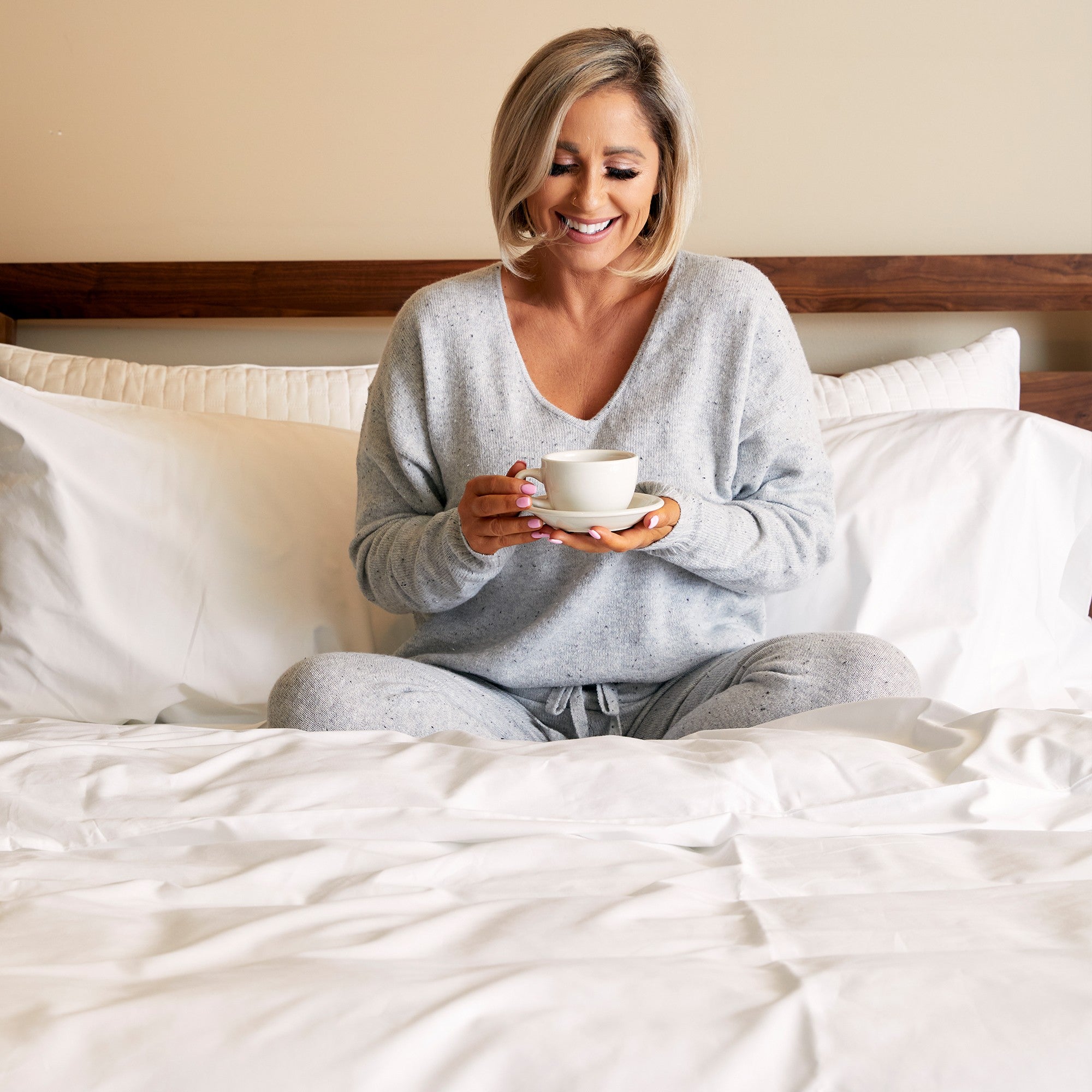 woman having coffee in bed on snow white bamboo sheets against pillows