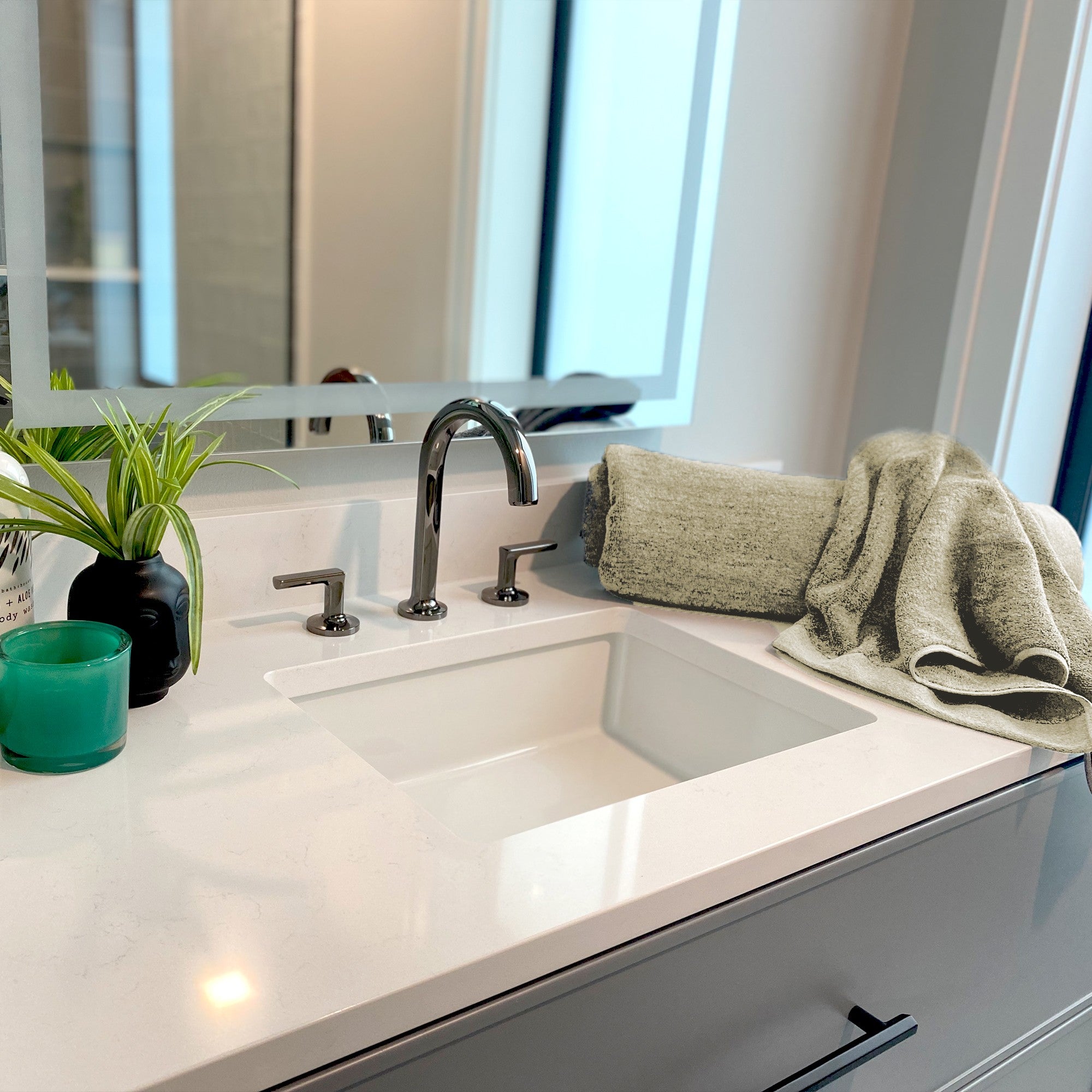 beige hand towels folded on a bathroom counter top with green plants and candle