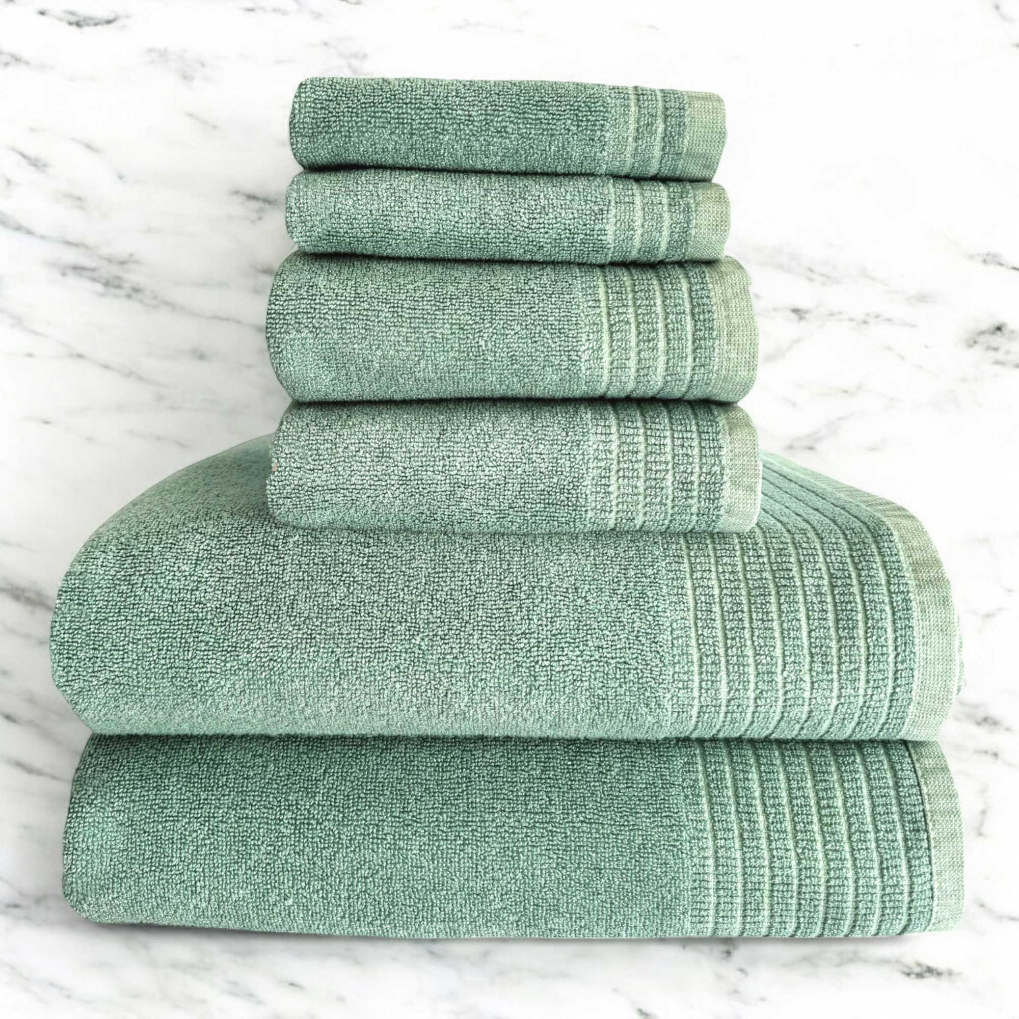 A set of folded green bamboo and cotton spa towels on a marble surface.