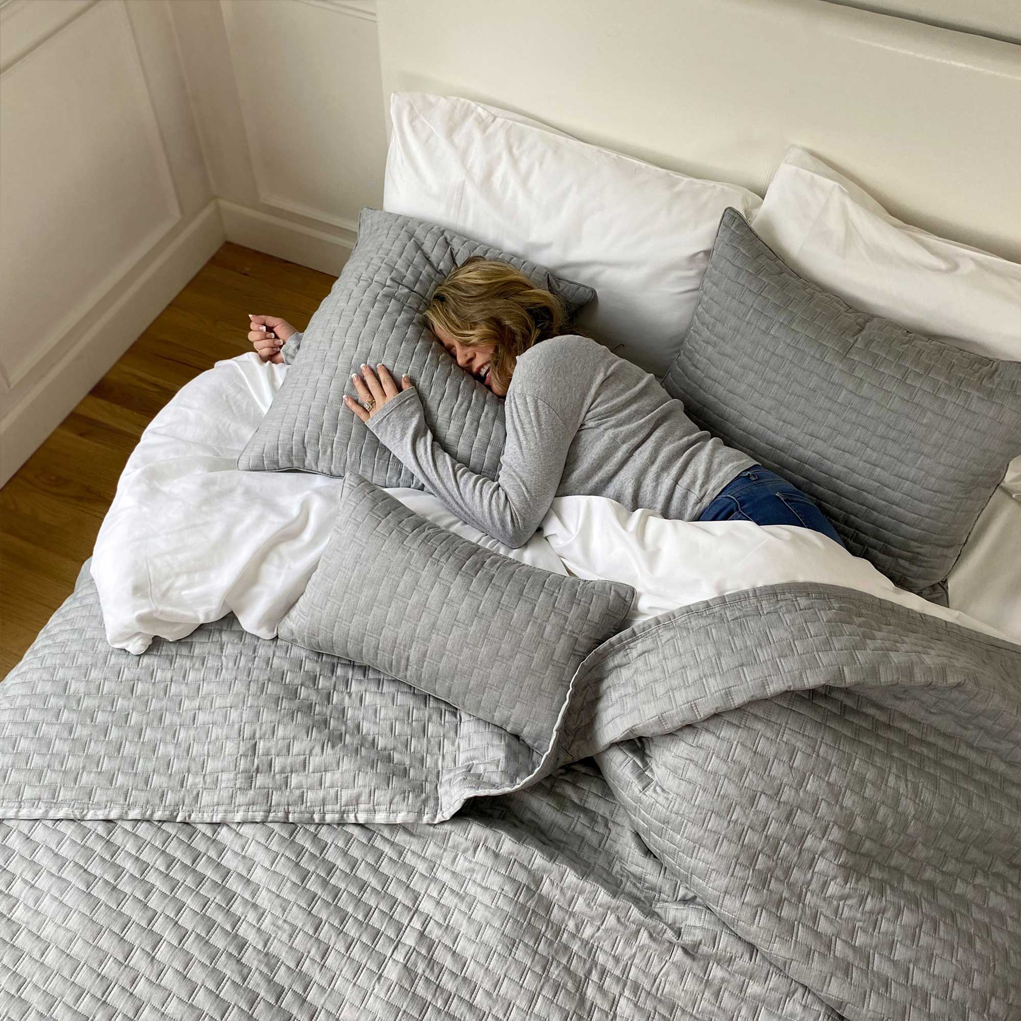 smiling woman laying on silver gray quilted melange bamboo coverlet and pillows