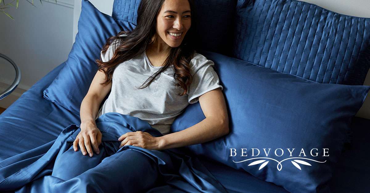 A smiling woman on bed with Bed Voyage logo in lower right hand corner