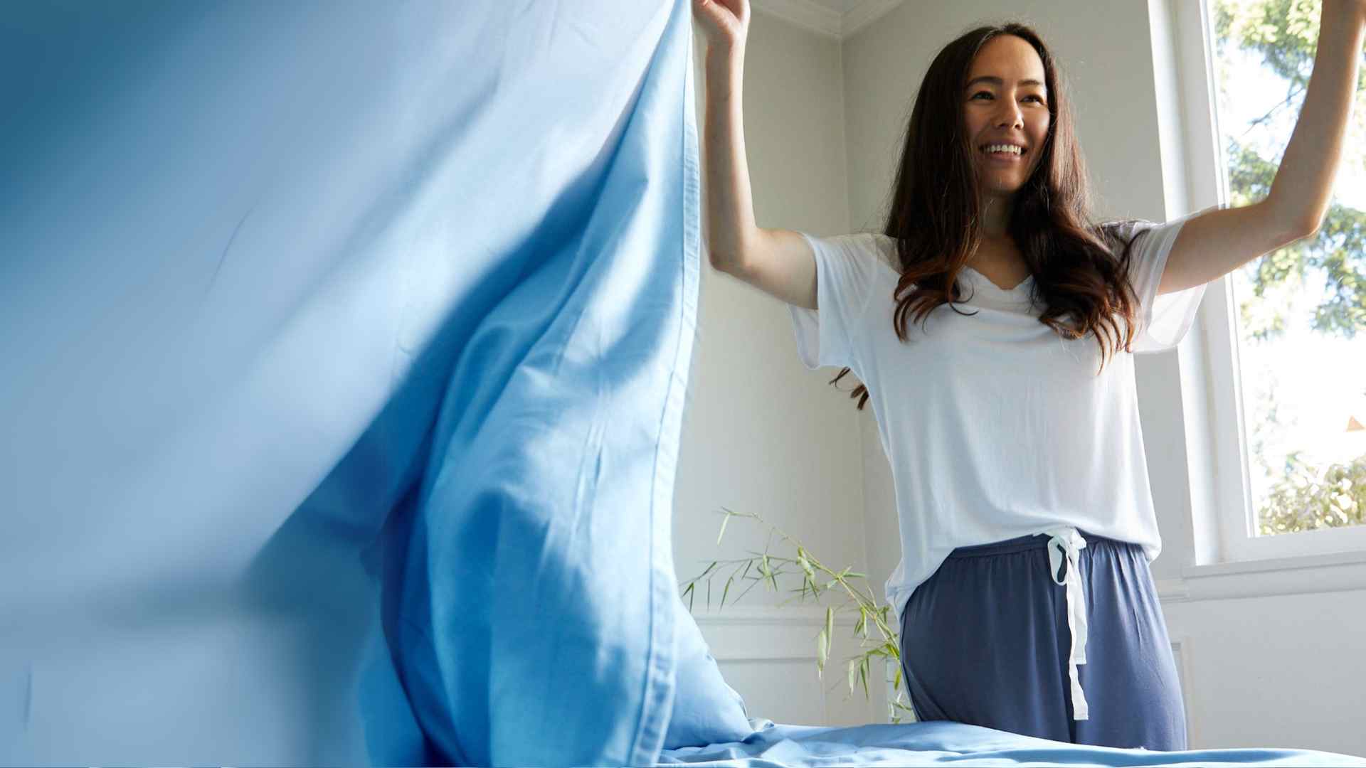Woman making bed with blue BedVoyage sheets