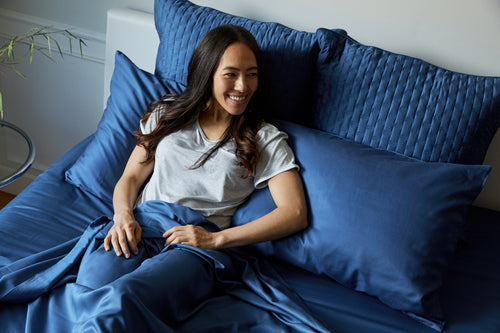 woman smiling in bed on dark indigo blue bamboo bed sheets and pillows