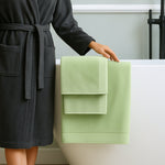 Person in a dark robe with a green towel draped over a bathtub