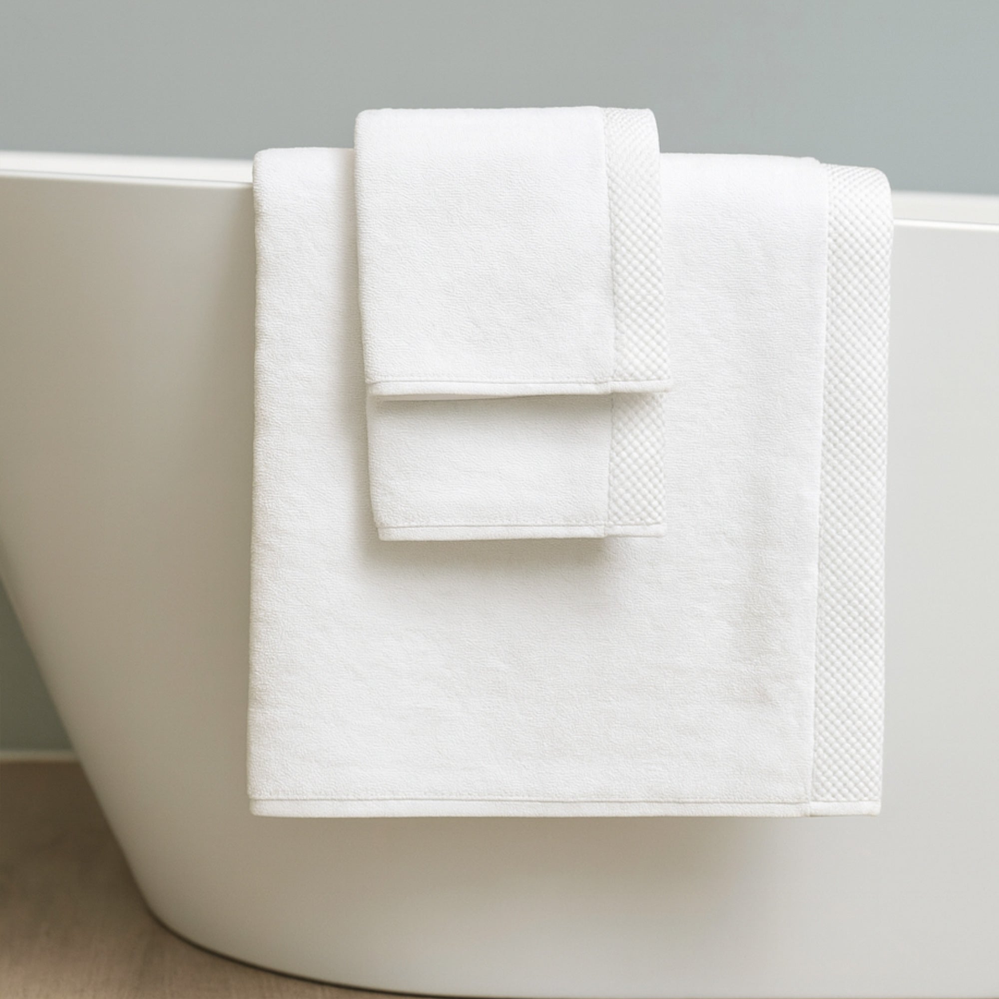 White bath towel draped over a white bathtub against a gray background