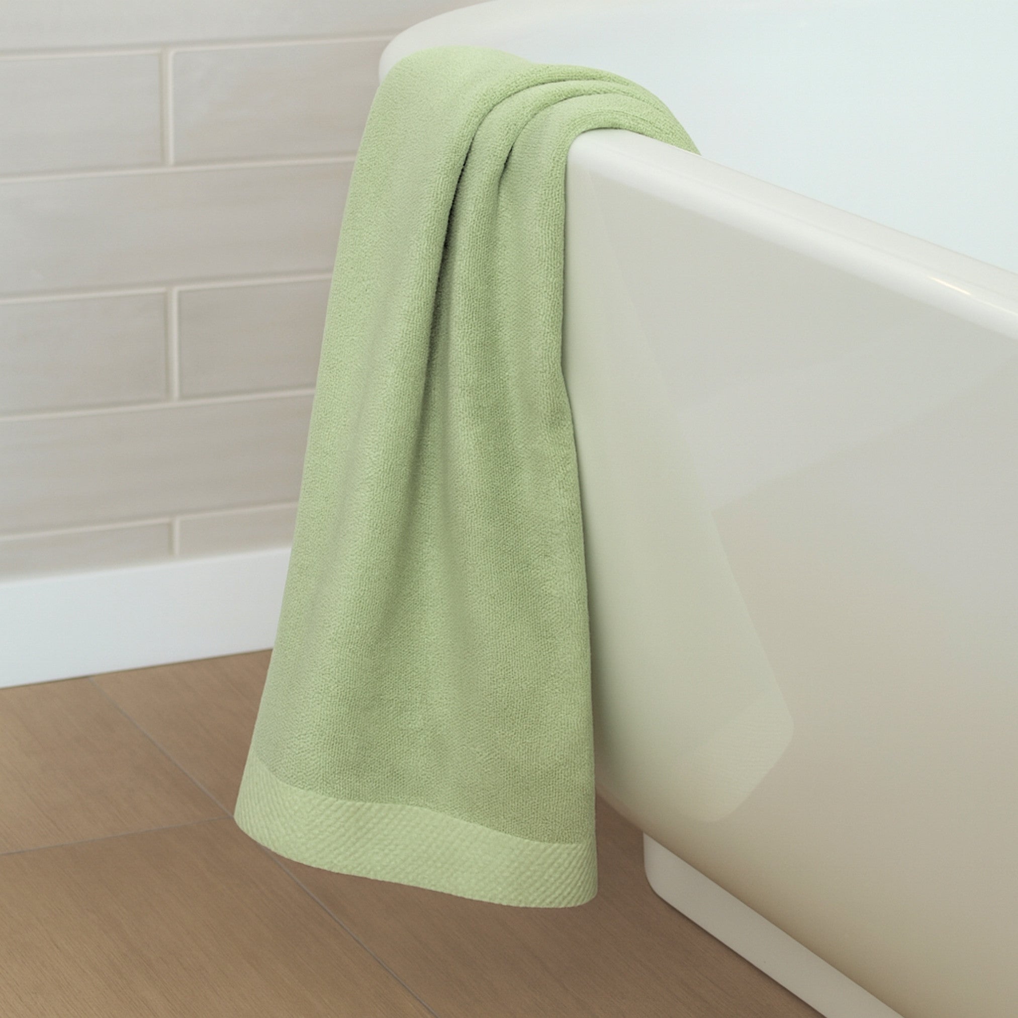 Green towel draped over a white bathtub in a bathroom setting
