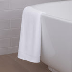 White bath towel draped over a white bathtub against a tiled bathroom wall.