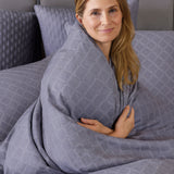 woman smiling wrapped in a gray and white geometric pattern duvet cover and pillows