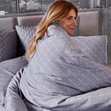 light haired woman wrapped in a gray geometric pattern bamboo duvet cover on a great bed