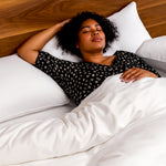 woman sleeping on white bamboo duvet cover and pillows, against wood headboard