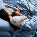 Woman lying in bed under blue sheets and pillows, wearing a white shirt.