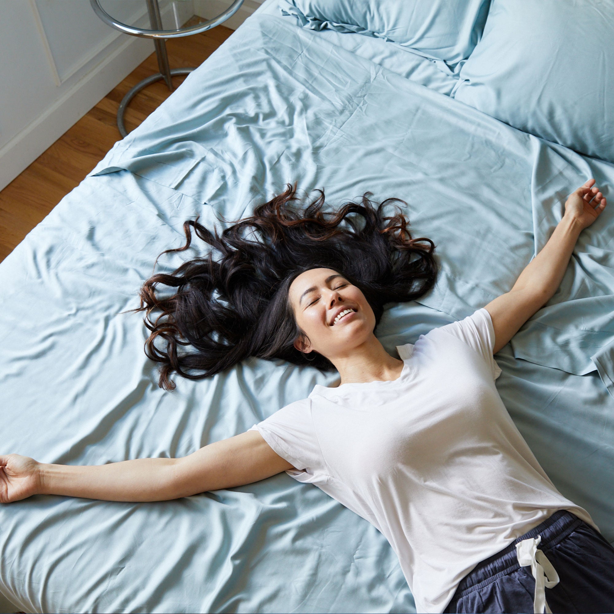 Woman lying on a bed with light blue bedding, smiling.