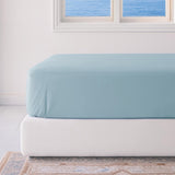 Light blue fitted sheet on a white bed in a room with a window.