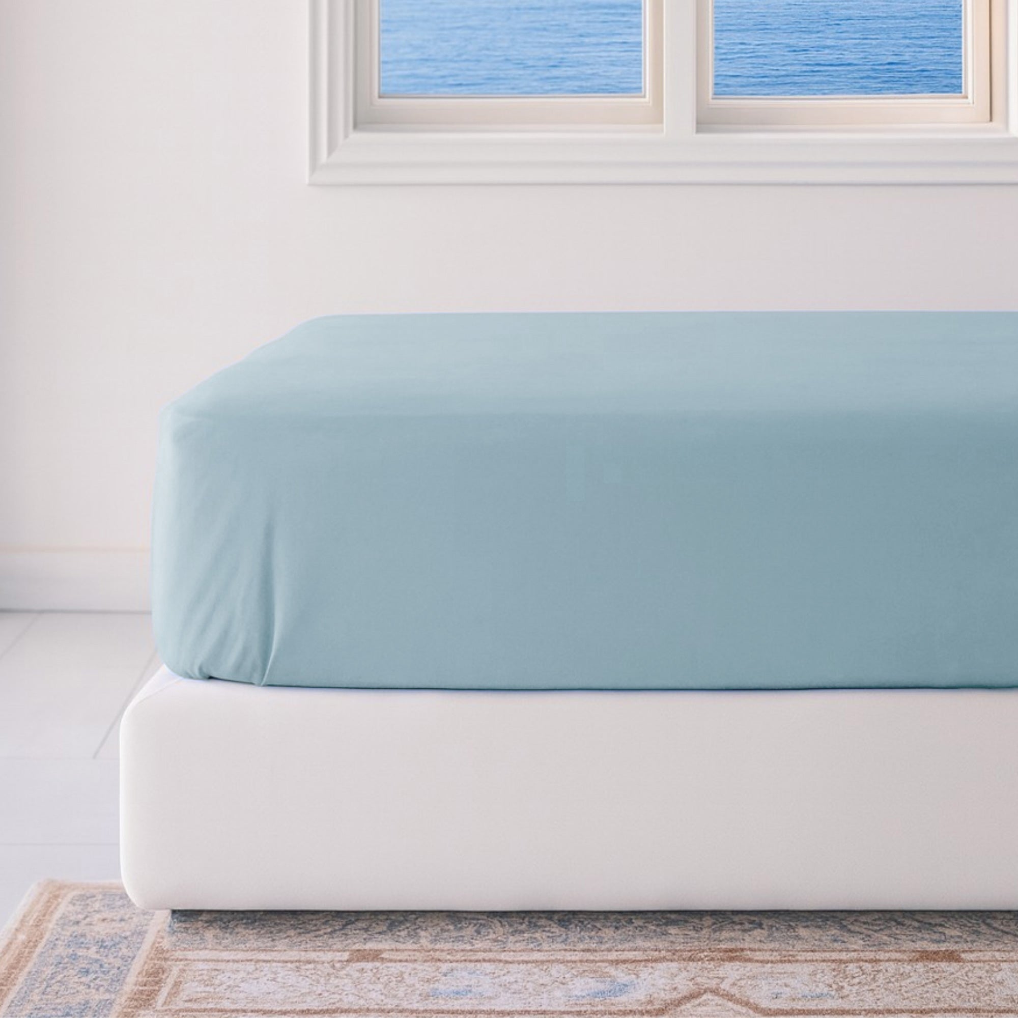 Light blue fitted sheet on a white bed in a room with a window.