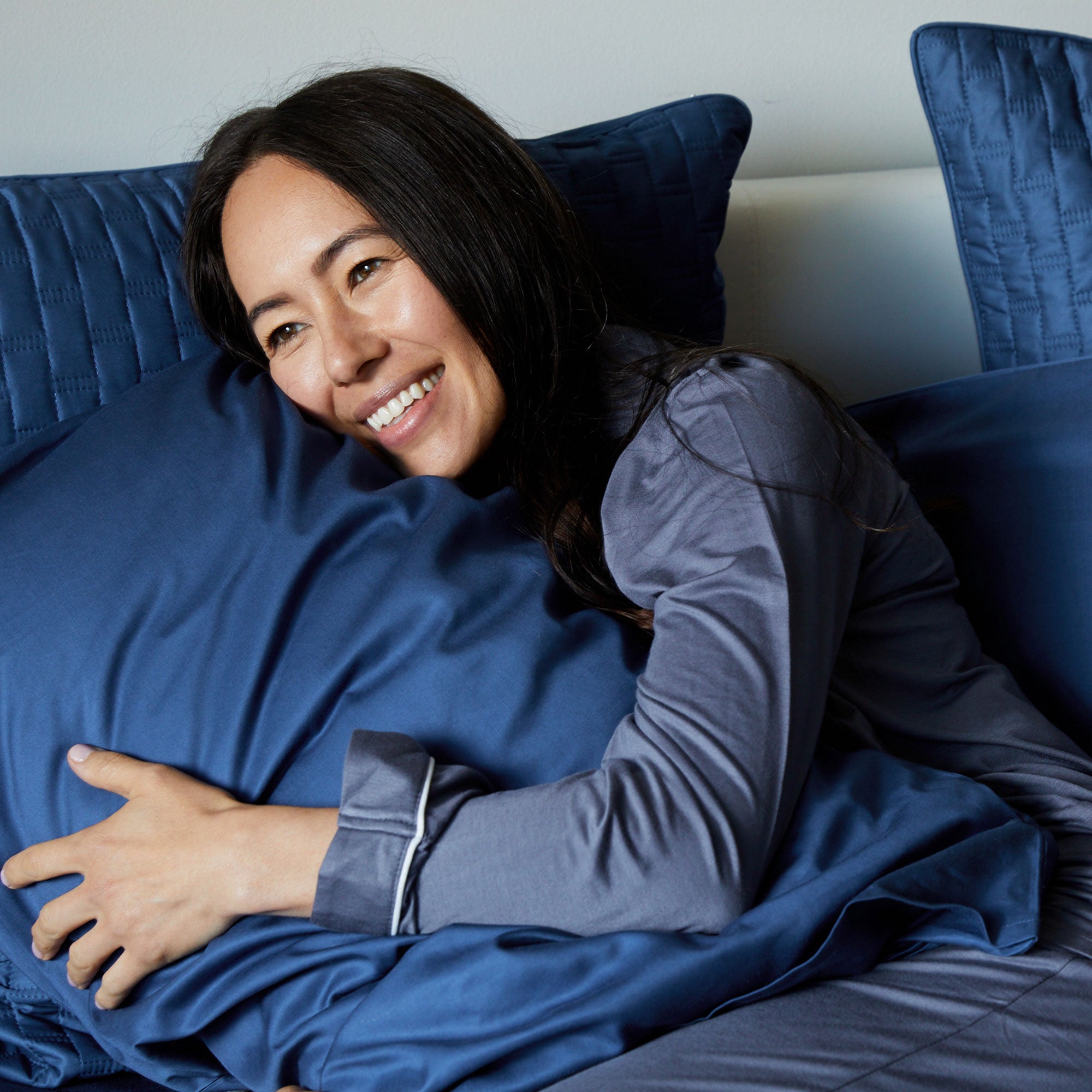 dark haired lady smiling in bed snuggling a dark blue indigo bamboo pillowcase in a pillow
