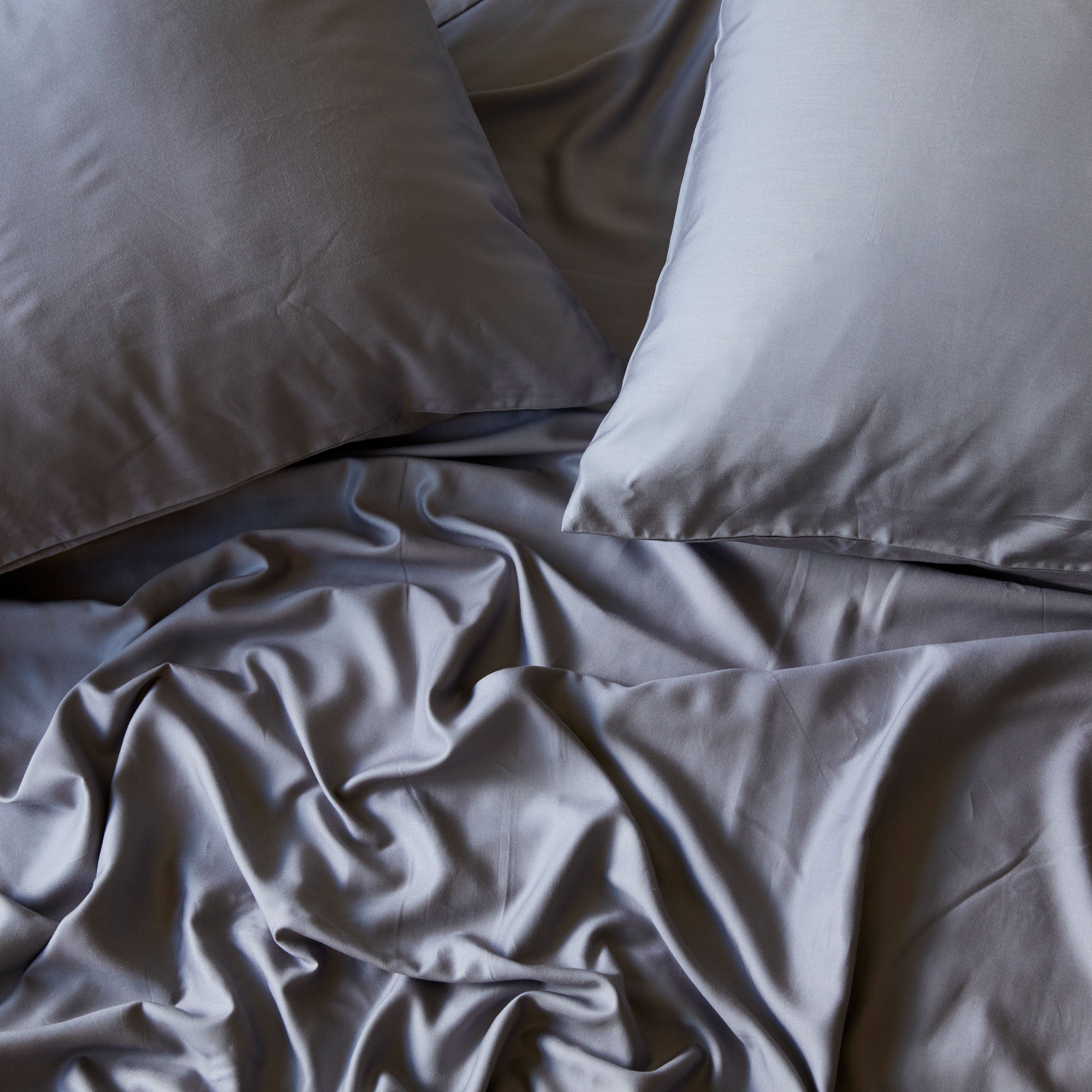 2 elegant pillows with dark gray bamboo pillowcases and flat sheet looking messy and luxurious