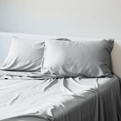 A set of stone gray bamboo pillowcases displayed on a bed, with two pillowcases visible in the foreground and a duvet cover in the background.