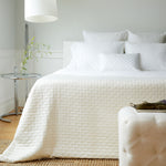 elegant bed in bedroom with ivory quilted bamboo coverlet and pillows with plants