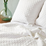 white quilted bamboo coverlet with euro shams on a bed with a glass jar and plant on side table
