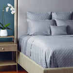 Bedroom with a neatly made bed featuring light gray bamboo bedding and pillows, next to a wooden nightstand with a plant.