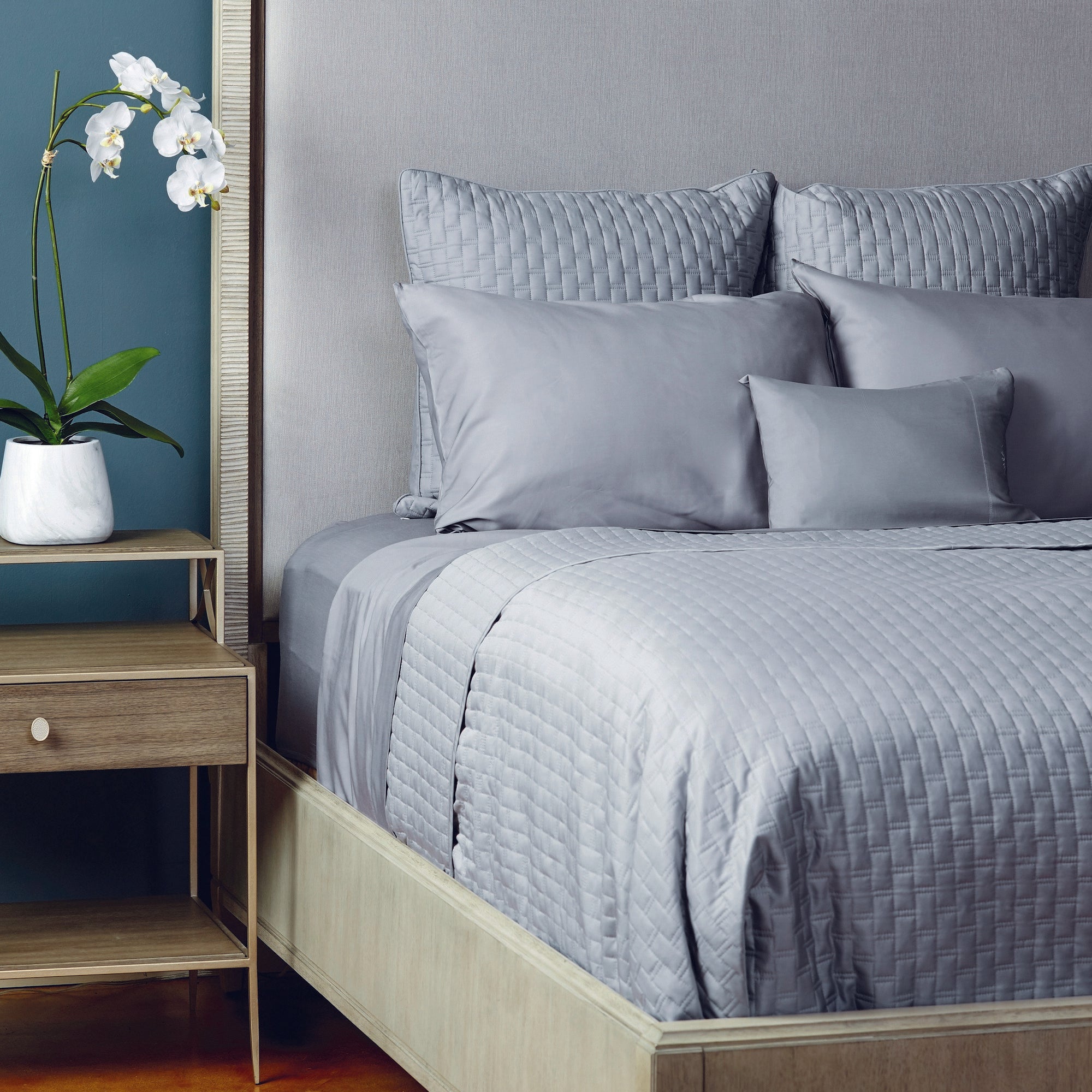 Bedroom with a neatly made bed featuring light gray bamboo bedding and pillows, next to a wooden nightstand with a plant.