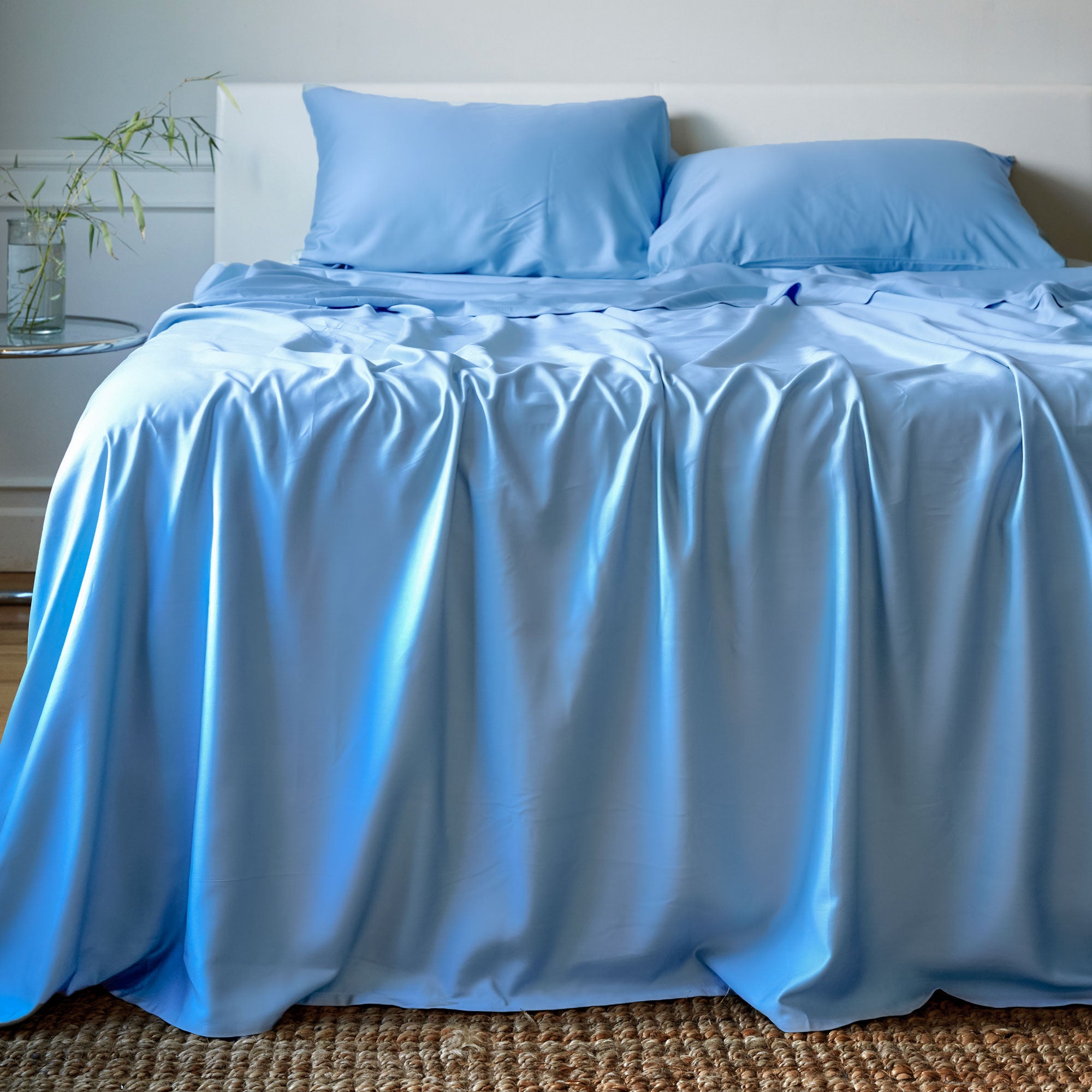 Blue bamboo bedding set on a bed with a white headboard and plant in the background.
