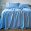 Blue bamboo bedding set on a bed with a white headboard and plant in the background.