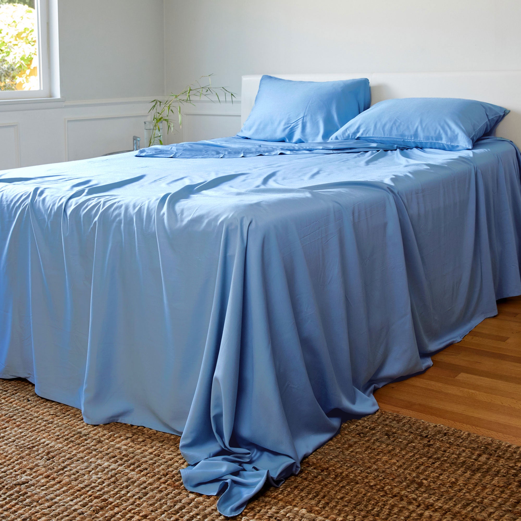 Bed with blue bamboo bedding in a room with a window and plant.