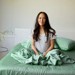 Woman sitting on a bed with green bamboo bedding and pillows.