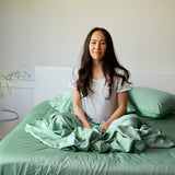 Woman sitting on a bed with green bamboo bedding and pillows.