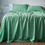 Green bamboo sheets and pillows on a bed in a room with a plant and table.
