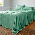 Green bamboo sheets and pillows on a bed in a room with a window and plant.