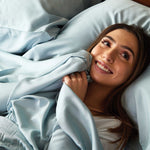 young lady smiling in bed on sky blue bamboo bed sheets snuggling with fitted sheet
