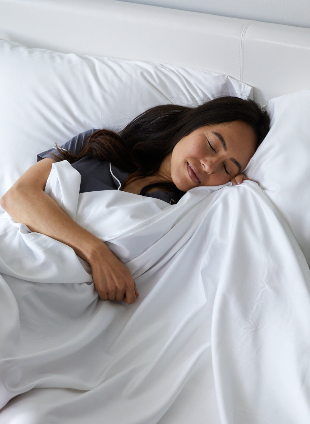 dark haired woman snuggling in bed with white bamboo sheets head on pillow