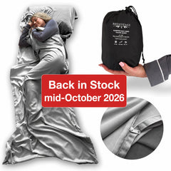 A gray satin sleep bag shown on a model lying down, alongside a hand holding the black drawstring storage pouch, a circular fabric detail inset, and a red text banner reading 'Back in Stock mid-October 2026'.